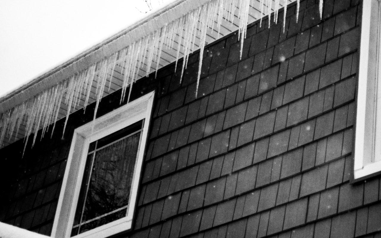 Icicles and an ice dam forming along the eaves of a shingled roof in winter